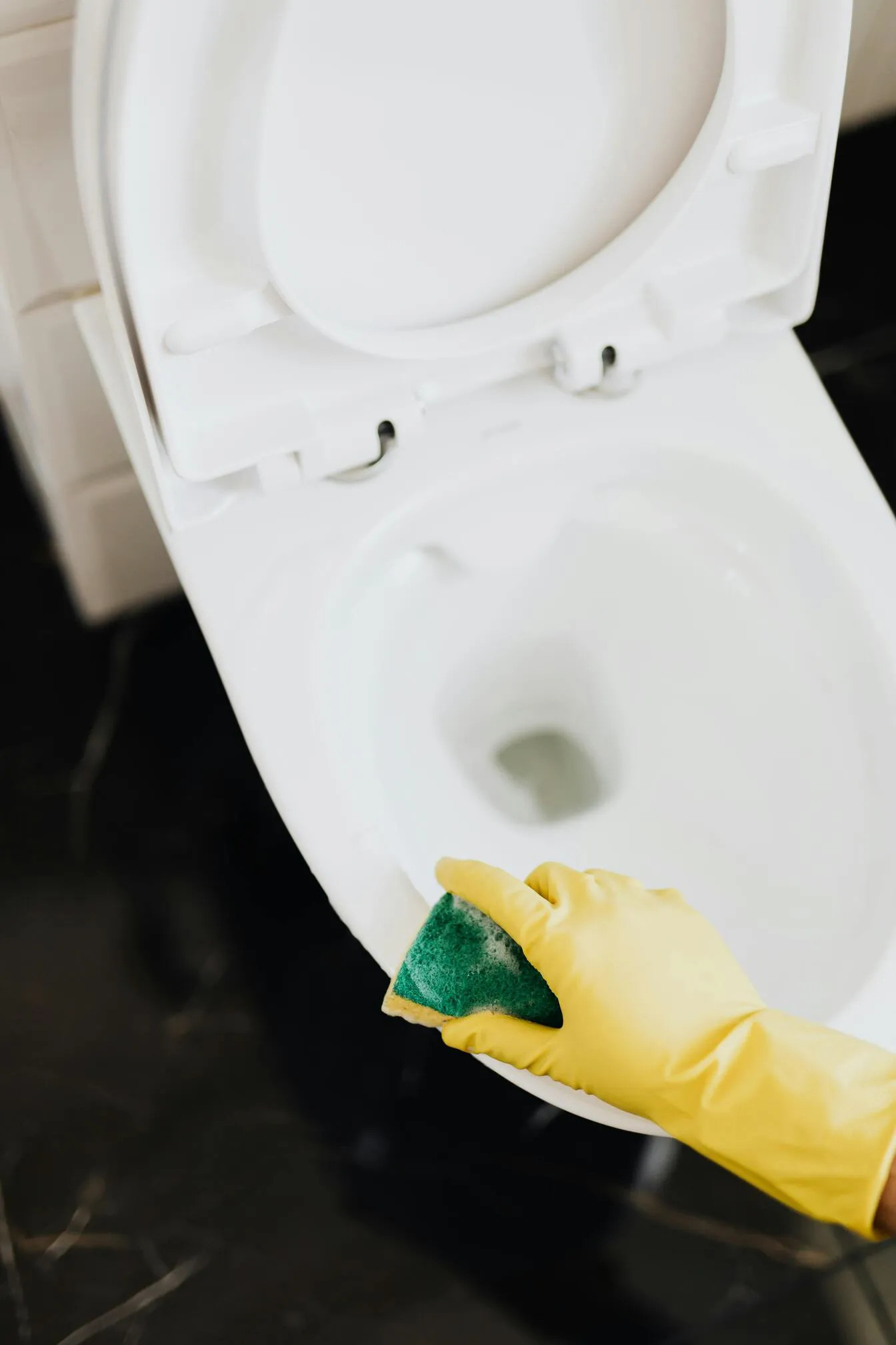 Cleaning toilet bowl with sponge and yellow gloves.