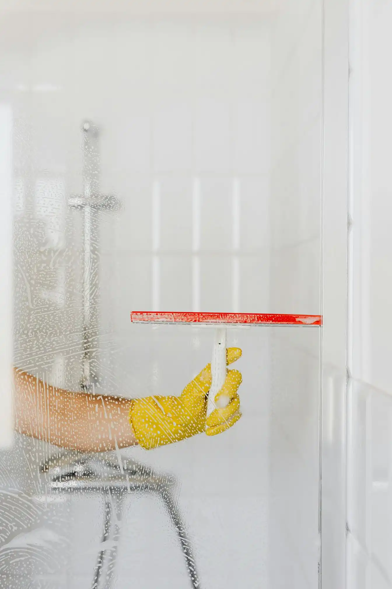 Wiping shower glass with squeegee and yellow gloves.